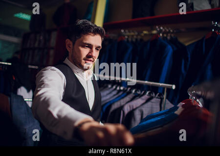 Tailor, tailoring. Men's suit, tailor in his workshop. Elegant man's suits hanging in row. Luxury mens classic suits on rack in elegant men's boutique. Stock Photo