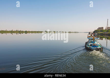 Small tug boat towing a yacht on nile river in Egypt through rural countryside landscape Stock Photo