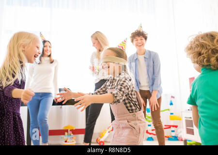 Excited blindfolded girl catching friends during game Stock Photo