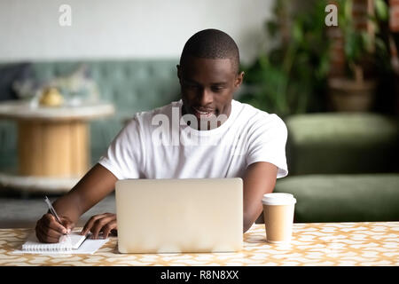 Smiling African American man using laptop, making notes Stock Photo