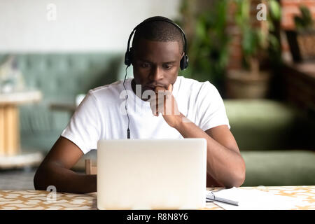 Focused African American man wear headphones, using laptop Stock Photo