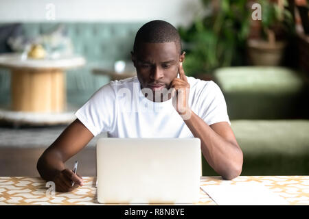 Focused African American man using laptop in cafe Stock Photo