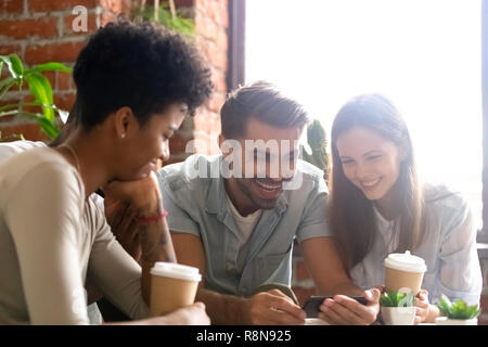 Happy diverse friends using phone together in cafe Stock Photo