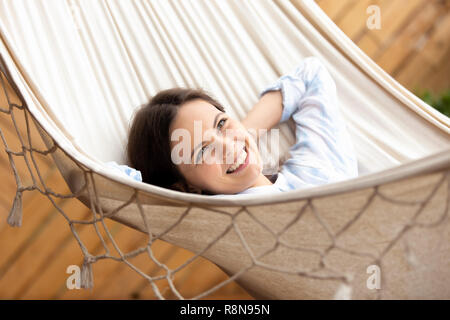 Happy smiling young woman lying in hammock looking in distance Stock Photo