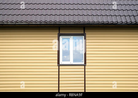 Building metal roof and wall finished with beige siding panels with white plastic window front view Stock Photo