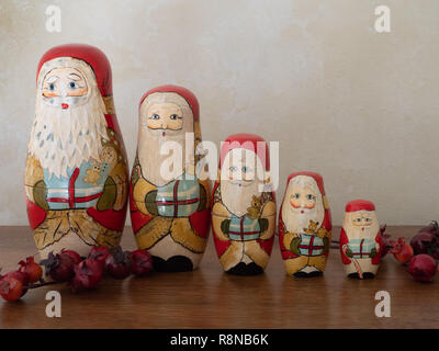 Five handpainted wooden nesting Santas in a row on a wooden table with red berries in the foreground. Photographed at eye level. Image has copy space. Stock Photo