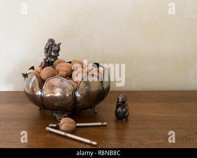 Tarnished decorative silver bow with mixed nuts, squirrel figurines with a walnut and nutcracker. Photographed at eye level. Copy space. Stock Photo