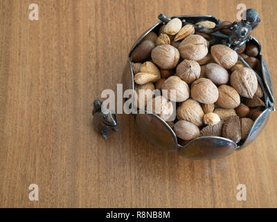 Silver bowl with two silver squirrel figurines  photographed on a wooden table from above. Bowl contained unshelled mixed nuts. Stock Photo