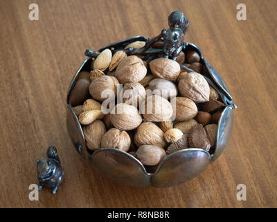 High angle view of a silver bowl with squirrel figurines. Mixed nuts with shells are in the bowl. Stock Photo