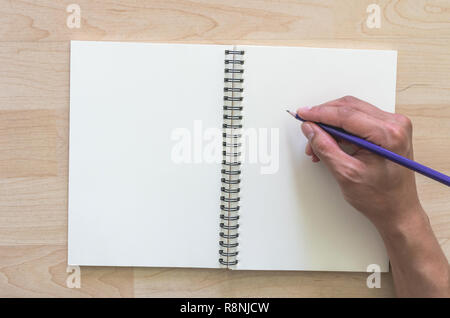 Hand holding Pencil and writing on the open leather book with wooden background Stock Photo