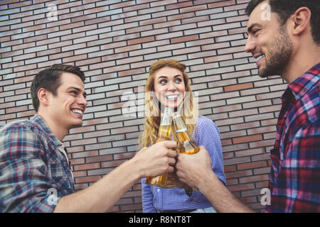 The three happy friends enjoying with beer on a brown brick wall background. Stock Photo