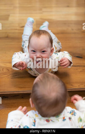 The reflection of a  nine month old baby girl looking in a mirror and smiling at the viewer Stock Photo
