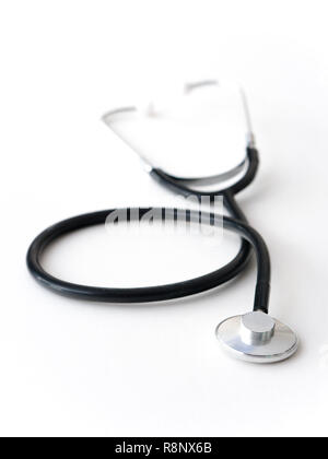 A doctors black flexible rubber and steel metal heart pulse stethoscope laying isolated on a white table top. Stock Photo