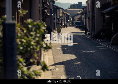 An elderly Japanese lady cycles down an elegant traditional street in Kyoto, Japan. Stock Photo