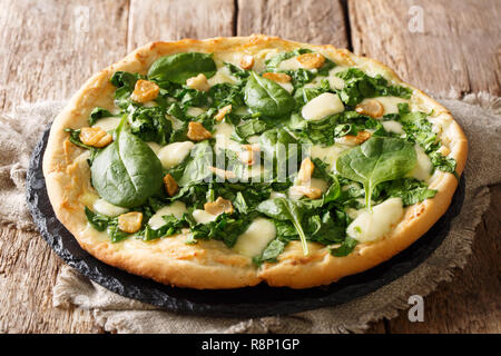 Italian white pizza recipe with fresh spinach, garlic and cheese close-up on a board on a table. horizontal Stock Photo