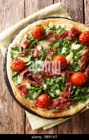 Italian white pizza with spinach, tomatoes, prosciutto and cheese close-up on the table. Vertical top view from above Stock Photo