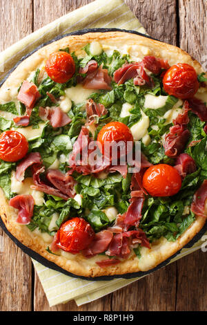 Pizza with spinach, tomatoes, prosciutto and cheese close-up on the table. Vertical top view from above Stock Photo