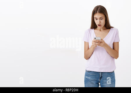 Portrait of shocked speechless and amazed good-looking young female smartphone owner dropping jaw from surprise staring with disbelief and amazement at cellphone screen reacting to shocking news Stock Photo