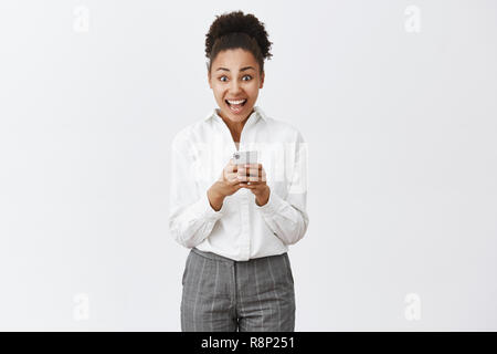 Girl being overwhelmed and excited reading incredible offer received via internet, checking mailbox in smartphone, staring amazed at camera, standing over gray background in suit Stock Photo
