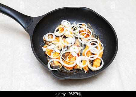 Fried fish in a frying pan with circles of onion Stock Photo