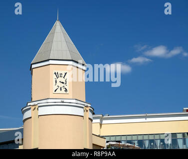 Modern style square clocks with black arabian digits shows quater pas three PM on tower with spire on beige facade city building under clear blue sky Stock Photo