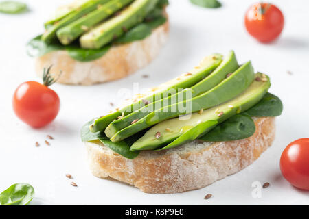 Two ciabatta toast with sliced avocado olive oil, spinach and flax and sesame seeds. Healthy vegetarian Breakfast on white background. Stock Photo