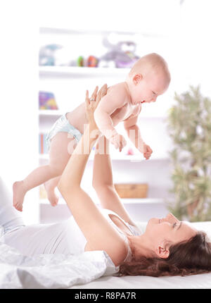 young mother plays with the baby lying on the bed Stock Photo