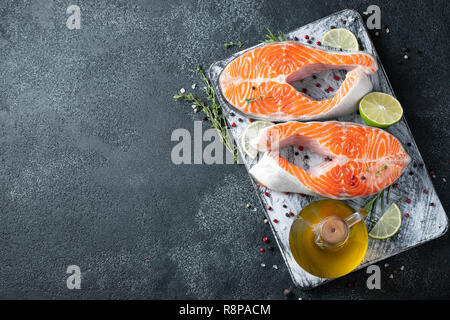 Two raw fresh salmon or trout steaks, rich in omega-3 oil, with lime, thyme and olive oil on a dark background. Healthy and dietary food. Top view with copy space. Flat lay Stock Photo