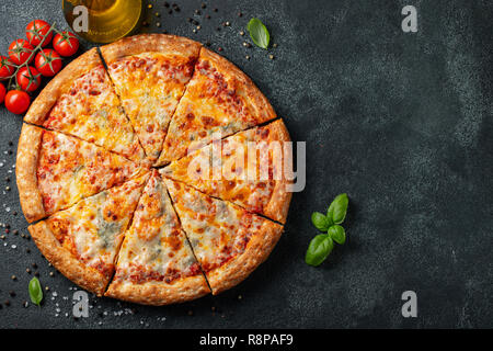 Delicious Italian pizza four cheeses with Basil, tomatoes and olive oil on a dark concrete table. Top view with copy space. Flat lay Stock Photo