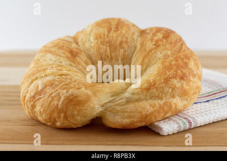 Single croissant roll on wooden cutting board with cloth.  Side view.  White background. Stock Photo