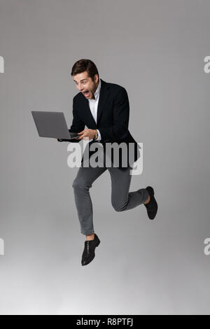 Full length image of joyous businessman 30s in suit rejoicing while using laptop isolated over gray background Stock Photo