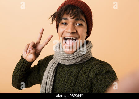 Portrait of a happy young african man dressed in autumn clothes isolated over beige background, taking a selfie Stock Photo