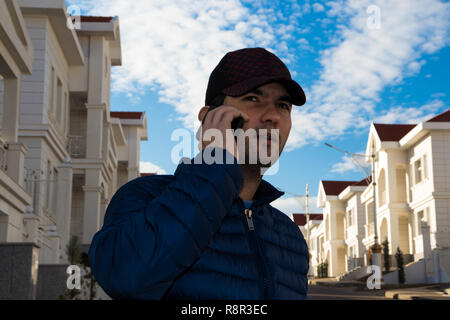 a real estate agent in front of residential villas having a conversation via mobile phone with a potential client on a background of a blue cloudy sky Stock Photo
