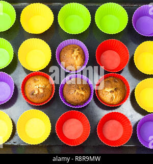 top view of few baked cupcakes and many empty multicolor silicone molds on dark tray Stock Photo