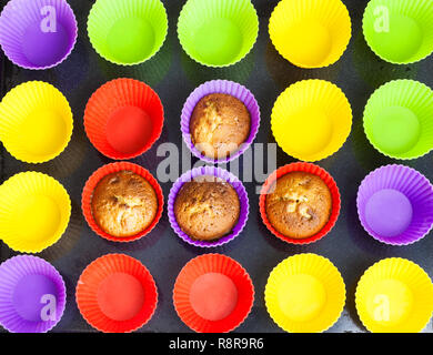 top view of four baked cupcakes and many empty multicolored silicone molds on dark tray Stock Photo