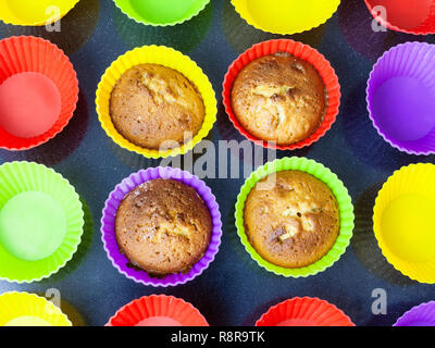 top view of four baked cupcakes in multicolored silicone molds on dark tray Stock Photo