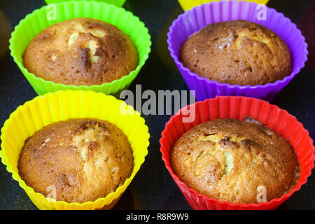 fresh baked cupcakes in multicolored silicone molds close up on dark tray Stock Photo