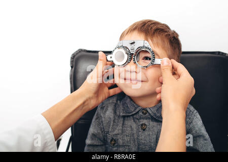 optometrist checking vision of a little cheerful boy using trial frame Stock Photo