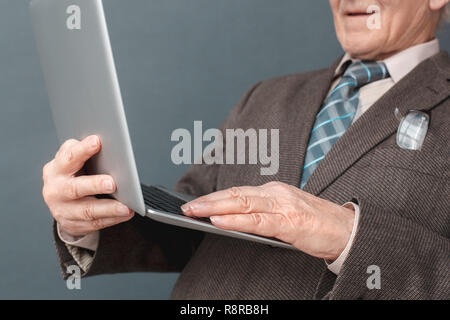 Senior man studio standing isolated on gray using laptop checking media smiling close-up Stock Photo