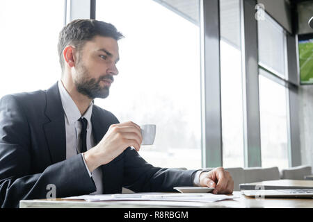 Businessperson on business lunch at restaurant sitting drinking coffee looking at laptop thougthful Stock Photo