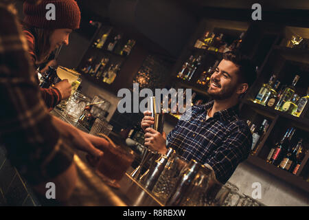 Young bartender standing at bar counter talking laughing with visitors cheerful Stock Photo