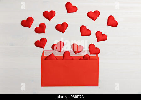 Closeup of red hearts flying out of a red paper envelope on a white wooden background. Valentine's day celebration concept Stock Photo