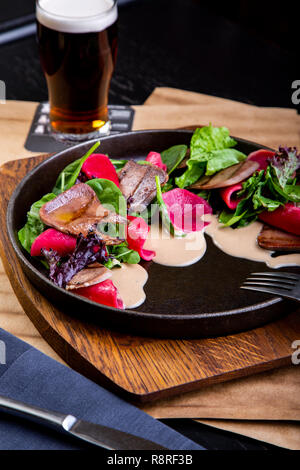 delicious beef tongue with spinach and beetroot in restaurant background. Healthy exclusive food on big black platter closeup Stock Photo