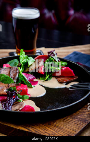 delicious beef tongue with spinach and beetroot in restaurant background. Healthy exclusive food on big black platter closeup Stock Photo
