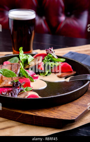 delicious beef tongue with spinach and beetroot in restaurant background. Healthy exclusive food on big black platter closeup Stock Photo