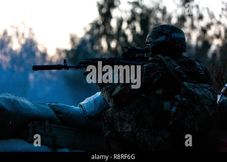 Sniper armed with large caliber, sniper rifle, shooting enemy targets on range from shelter, sitting in ambush. Side view Stock Photo