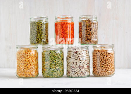 Mung beans, peas, beans, lentils and chickpeas in stacked glass storage jars over a white wall background rich in protein, dietary fiber and vitamins Stock Photo