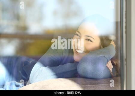 Happy lady looking through the window lying on a couch at home Stock Photo