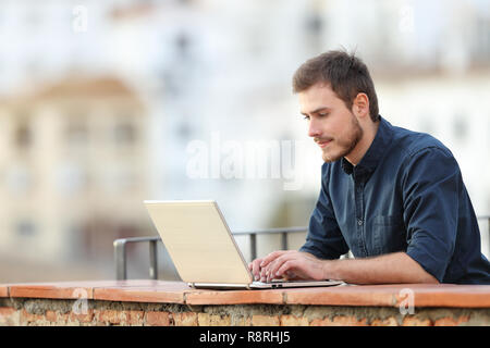 Concentrated writer writing on a laptop in a balcony on vacation in a town Stock Photo