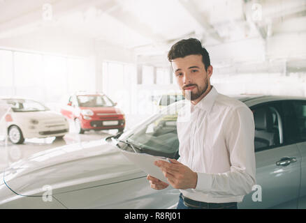 friendly vehicle salesman presenting new cars at showroom. Photo of young male consultant showing new car in auto show. Concept for car rental. Stock Photo